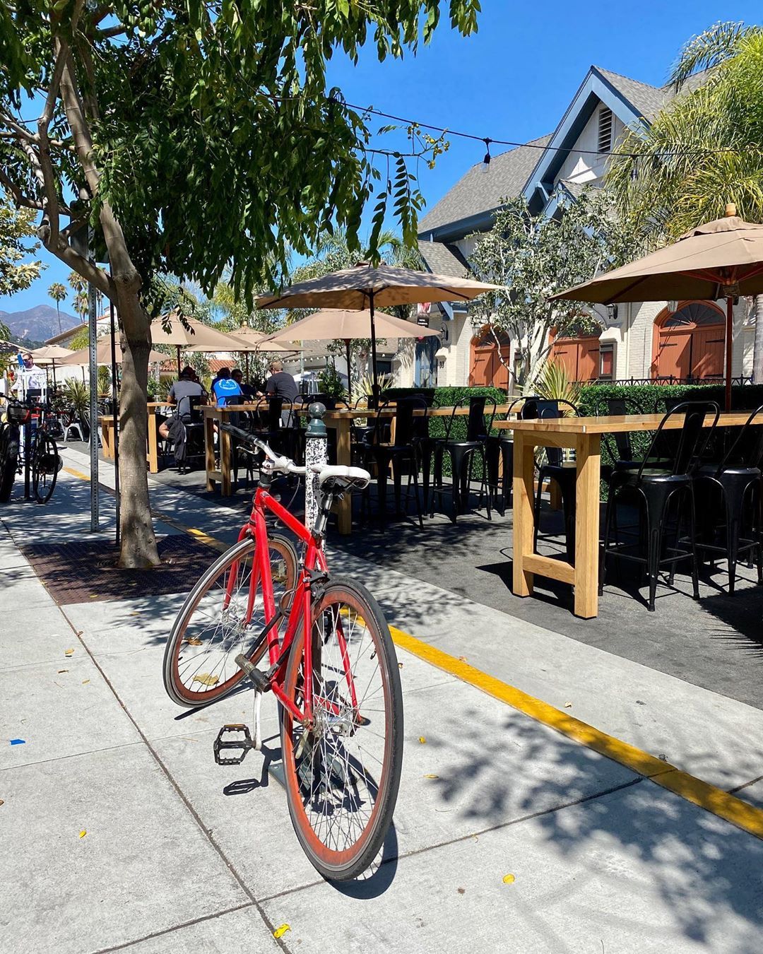 Tables, chairs, umbrellas on a restaurant's outdoor patio with a red bicycle in front